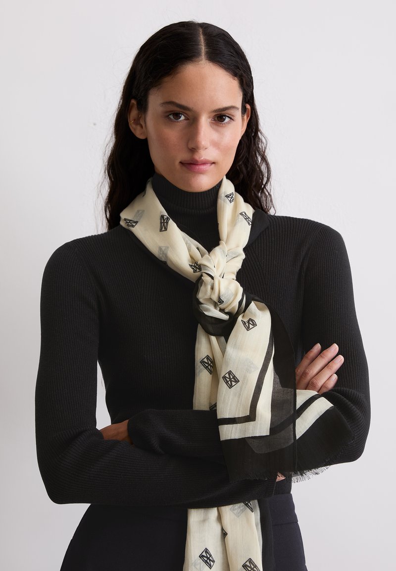 Sciarpa leggera color crema con motivo geometrico nero e bordo rifinito. Tessuto strutturato che cade elegantemente intorno al collo.