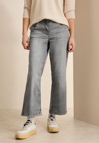 Jean large gris avec une finition délavée, présentant un design classique à cinq poches. Associé à des baskets blanches et des chaussettes à motifs.