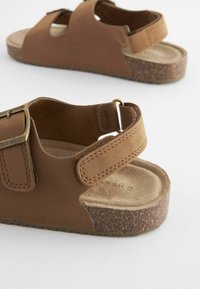 Bruna sandaler med övre i mockaliknande material, justerbara remmar och korksål. Har en metallspänne och en strukturerad fotbädd.