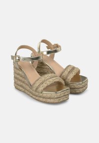 I sandali wedge dorati presentano una piattaforma in paglia intrecciata, cinturini metallici e una fodera interna liscia. Chiusura con fibbia alla caviglia.