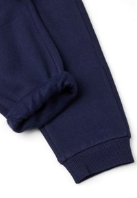 Pantaloni tuta blu navy con polsino elastico e morbido rivestimento in pile visibile all'orlo piegato.