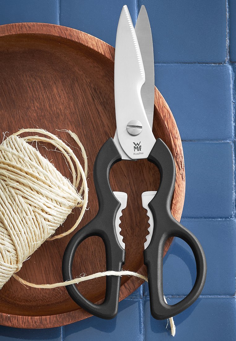 Tijeras de cocina de acero inoxidable con mangos ergonómicos negros, borde serrado, colocadas sobre un plato de madera al lado de cuerda.
