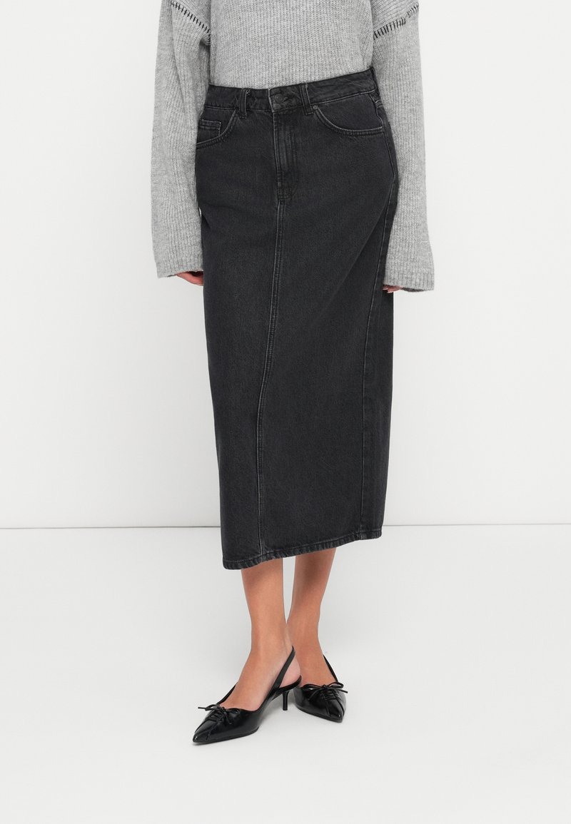 Črna denim midi krila s prilegajočim pasom, sprednjimi šivi in žepi. V kombinaciji z sivo pleteno puloverjem in črnimi petami na mule.