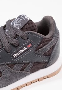 Szary but sportowy wykonany z teksturowanych materiałów, z siateczką i skórzanymi dodatkami, na białej podeszwie. Na języku znajduje się etykieta z logo przedstawiającym Union Jack.