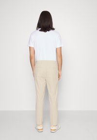 Pantaloni beige con taglio dritto, abbinati a una maglietta bianca e sneakers chiare. Tessuto liscio; nessun motivo o accentuazione visibili.