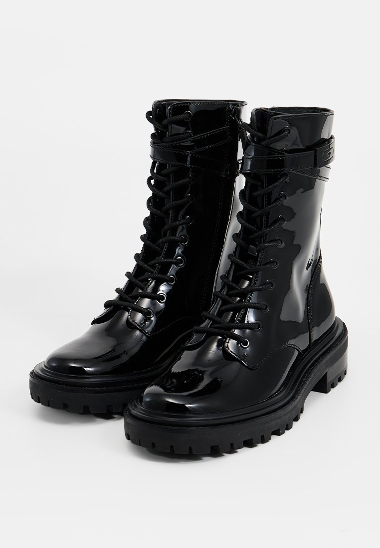 Schwarze Lackleder-Kampfstiefel mit runden Zehen, Schnürung vorne und strukturierten Gummisohlen. Mit Schnallenakzenten am Knöchel.