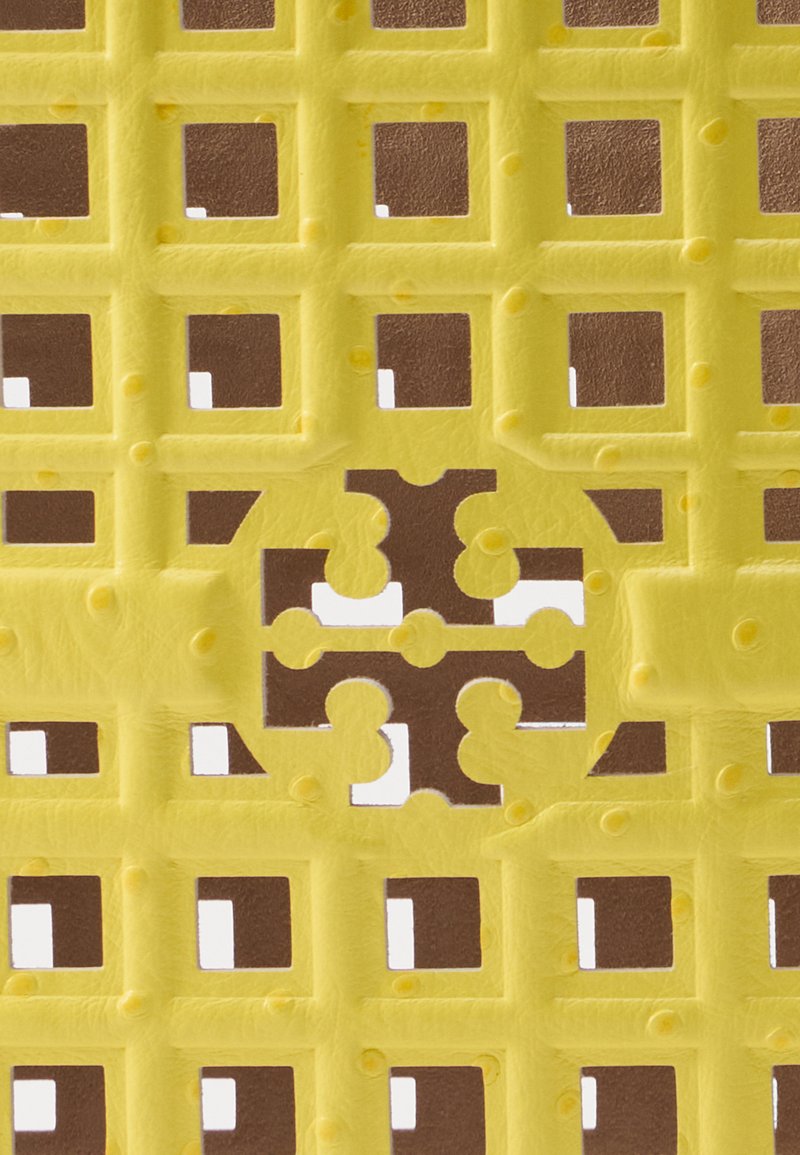 Gelbes strukturiertes Material mit einem Gittermuster, das ausgeschnittene Formen in Braun aufweist. Das Design enthält erhabene Punkte innerhalb der Gitterkästchen.
