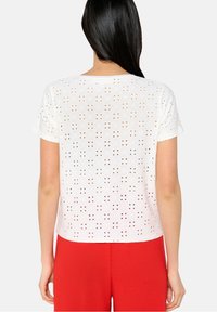 T-shirt bianca in cotone con motivi ritagliati, maniche corte e scollatura rotonda. Abbinata a pantaloni rossi brillanti.
