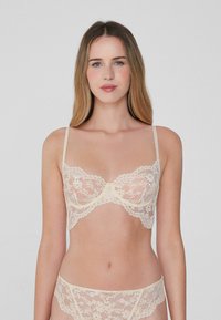 Krajkový bralet a odpovídající kalhotky v jemné béžové barvě. Nastavitelné ramínka, zvlněné okraje, květinový vzor, poloprůsvitná látka, podprsenka s kosticemi.