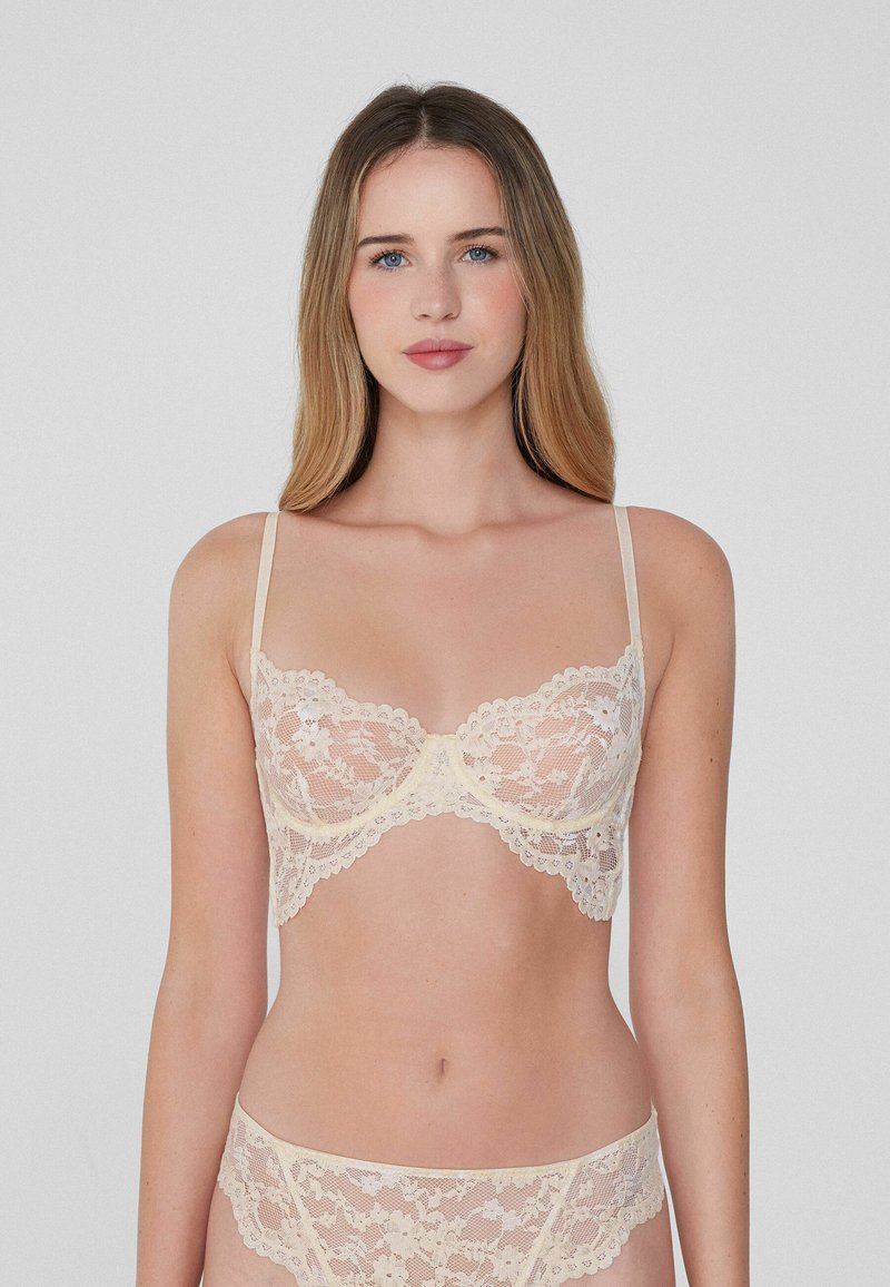 Krajkový bralet a odpovídající kalhotky v jemné béžové barvě. Nastavitelné ramínka, zvlněné okraje, květinový vzor, poloprůsvitná látka, podprsenka s kosticemi.