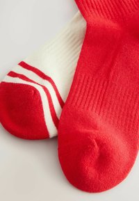Punased ja valged sokid. Üks on ühtlane punane, teine aga valge punaste triipudega ääres. Materjal näib olevat kootud ja pehme tekstuuriga.