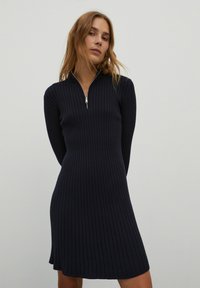 Marineblaues geripptes Kleid mit hohem Kragen und silbernem Reißverschluss, figurbetonte Silhouette, strukturiertes Gewebe und knielanger Rock.