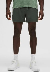 Mörkgröna sportshorts i lätt material, tillsammans med vita sneakers och ankelsockor, visade på en neutral bakgrund.