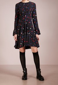 Svart långärmad klänning med röda, blåa och vita prickar, plisserad bodice, volangkant, ihopparad med knähöga svarta strumpor och svarta stövlar.