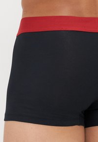 Schwarze Boxershorts mit einem roten elastischen Bund, ausgestattet mit einer glatten Textur und einer engen Passform, die für Komfort und Unterstützung sorgen.