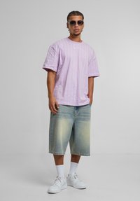 Chemise à manches courtes de couleur mauve clair avec des rayures blanches verticales, associée à un short en denim bleu clair surdimensionné et des baskets blanches.