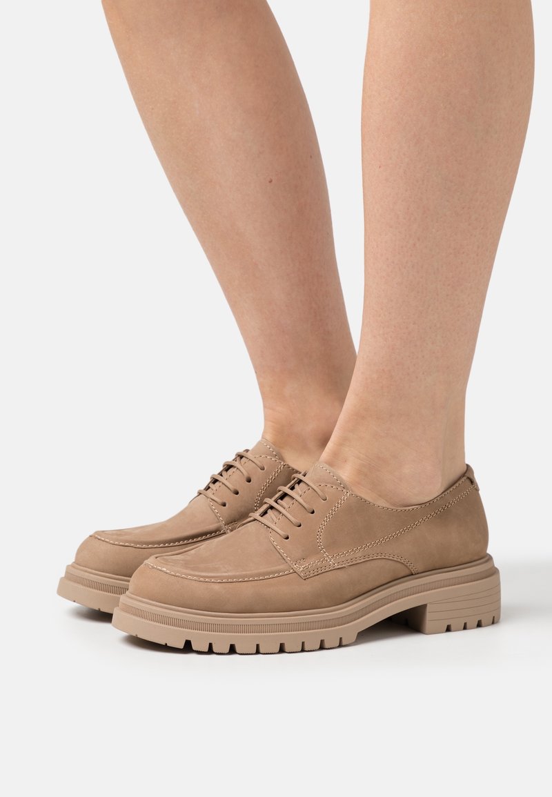 Chaussures à lacets en cuir marron clair avec un bout rond, une surface texturée et une semelle en caoutchouc épaisse rainurée. Détails de couture minimale sur la tige.