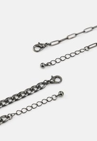 Cadeias de metal com acabamento escuro, apresentando vários elos, fechos tipo lagosta e contas decorativas. Comprimentos e texturas variados são visíveis.