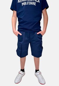 T-shirt in cotone blu navy con testo "AERONAUTICA MILITARE"; pantaloni cargo blu navy con tasche laterali; sneakers bianche con accenti rossi.