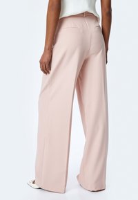 Wijde pijpen broek in zacht roze stof. Bevat twee achterzakken en een nette tailleband. Soepele textuur met een comfortabele pasvorm.
