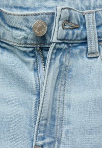 Los vaqueros de mezclilla de un azul claro cuentan con un cierre de botón metálico, una cremallera y detalles de costura en contraste a lo largo de las costuras.