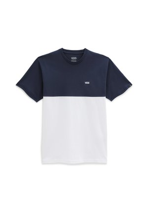 Personne portant un t-shirt Vans bleu marine et blanc, un pantalon noir, des baskets Vans noires, et un tatouage sur l'avant-bras gauche, debout devant un fond blanc.