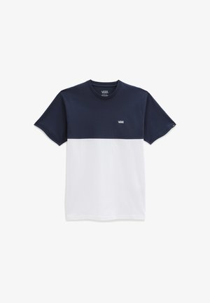 Personne portant un t-shirt Vans bleu marine et blanc, un pantalon noir, des baskets Vans noires, et un tatouage sur l'avant-bras gauche, debout devant un fond blanc.