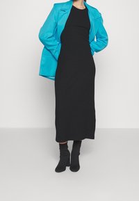 Černé žebrované midi šaty v kombinaci s oversized jasně modrou blázerem, doplněné o černé přiléhavé kotníkové boty. Čistý, moderní vzhled.