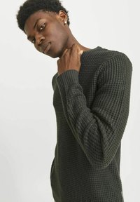 Maglione lavorato a maglia di un verde scuro con una superficie testurizzata e polsini a coste. Presenta un colletto tondo e tasche laterali.