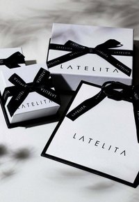 Three white gift boxes with black ribbon, displaying the brand name "LATELITA" in bold letters, featuring varying sizes and textures.