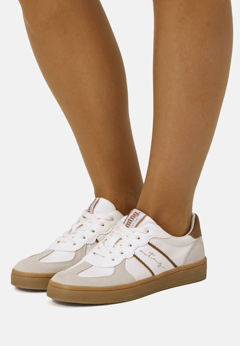 Zapatillas blancas con diseño en ante y cuero sintético. Incluyen detalles en marrón, cierre de cordones y suela de goma texturizada.