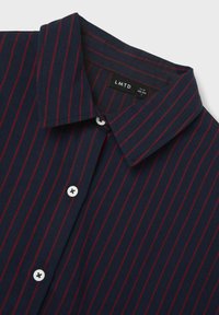 Camicia button-up a righe blu navy con sottili righe rosse. Realizzata in tessuto dalla superficie liscia. Bottoni bianchi e colletto classico.