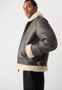 Μπουφάν από γούνα με γκρι εξωτερικό, κρεμ αποσπώμενη γούνα στον γιακά και τα μανίκια, δερμάτινες λεπτομέρειες, φερμουάρ στο μπροστινό μέρος και πλαϊνές τσέπες.