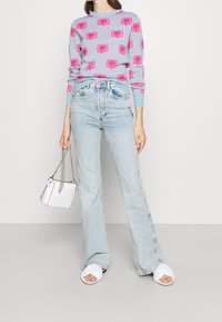 Ljusblå tröja med mönster av rosa pratbubblor, i kombination med högmidjade ljusblå jeans. Vit handväska med kedjesnodd och vita sandaler.