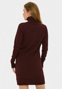 Bordo pulover obleka iz mehkega pletenega materiala. Ima dolge rokave, rebraste manšete in rob, ter oprijet kroj.
