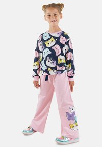 Kinder-Loungewear mit einem navyfarbenen Langarmshirt, das mit bunten Katzenköpfen bedruckt ist, und rosafarbenen weitem Hosen mit Katzenmotiven an der Seite.