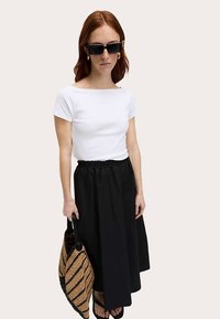 Biała dopasowana koszulka, czarna spódnica do kostek, słomiana torba. Dodatki to duże czarne okulary przeciwsłoneczne i złote kolczyki koła.