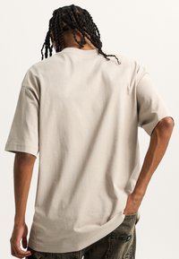 Camiseta oversized beige con cuello redondo, mangas cortas y una textura suave, vista desde la parte de atrás, destacando un ajuste relajado.