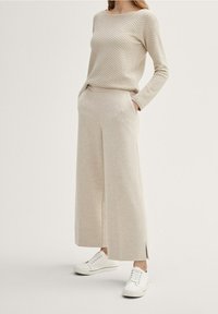 Beige texturerad tröja med långa ärmar, ihop med beige vida byxor med sidoslitsar, kompletterat med vita sneakers.