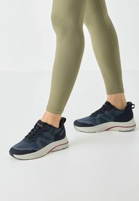 Scarpe sportive in navy con dettagli grigi chiari. Caratterizzate da una suola ammortizzata e una tomaia testurizzata. Abbinato a leggings oliva a costine.