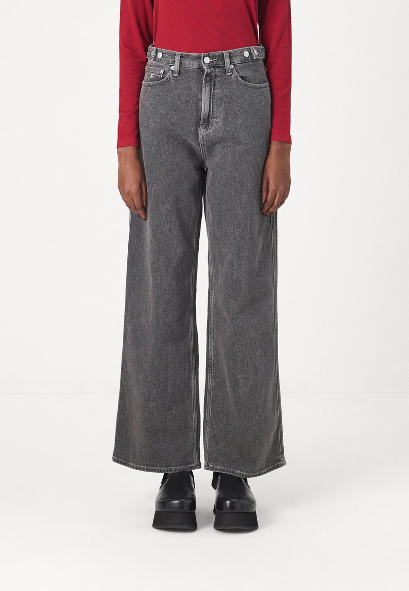 Hellegrau weit geschnittene Jeans mit hoher Taille, fünf Taschen, Metallknöpfen und einem leichten Verwaschungseffekt. Kombiniert mit klobigen schwarzen Plateauschuhen.