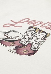 Grafikai tervezés vörös és fehér cowboy csizmákkal, valamint egy fehér cowboy kalappal, rózsaszín hímzett "Levi's" szöveggel.