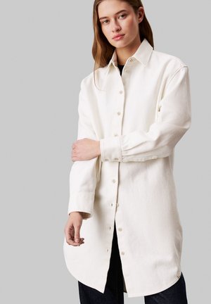 Camicia bianca a maniche lunghe con bottoni, realizzata in tessuto texturizzato, con colletto classico, taglio dritto e orlo dritto.