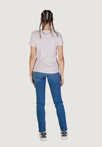 Roze katoen T-shirt met korte mouwen, gecombineerd met strakke blauwe denim jeans en geprinte witte sneakers. Achteraanzicht van de outfit.
