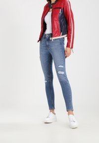 Chaqueta de cuero roja y azul marino con rayas blancas, combinada con jeans ajustados desgastados de color azul claro y zapatillas blancas.