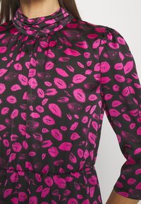 Zwarte stoffen jurk met een print van roze lippenmotieven. Heeft een hoge hals, pofmouwen en een geplooide taille. Zacht, textuurachtig materiaal.