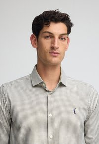 Camicia da uomo con bottoni, caratterizzata da un motivo a quadri verdi e bianchi, maniche lunghe, colletto e un piccolo logo ricamato sul lato sinistro del petto.