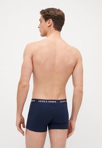 Tamno plave pamučne bokserice s elastičnom trakom na kojoj je logotip "JACK & JONES". Glatka tekstura, prilagođeni oblik, vidljiv stražnji dio.
