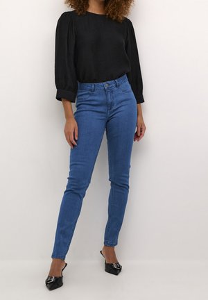 Blouse noire texturée à manches bouffantes associée à un jean slim taille haute bleu et des mules noires à talons pointus.
