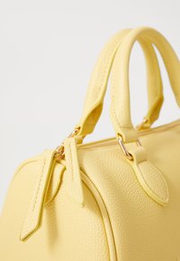 Borsa a mano gialla in pelle con superficie testurizzata, doppie maniglie e finiture in tono oro; presenta un'apertura con zip e dettagli decorativi.